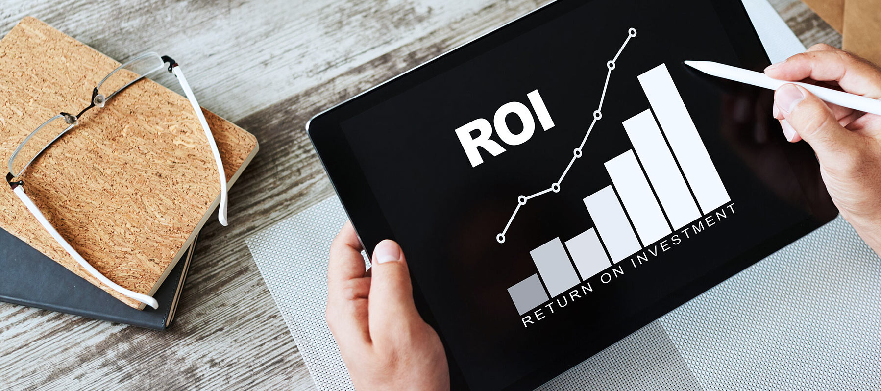 Close-up of a businessman's desktop with hands holding a tablet showing a chart, highlighting the concept of ROI in business.